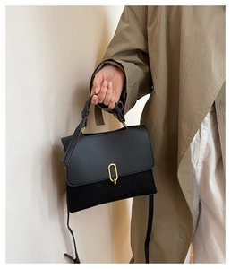 Detail of black crossbody bag with leather stitching and gold buckle on a model