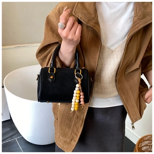 Detail der schwarzen Mini-Boston-Tasche mit goldener Hardware und buntem Holzperlen-Quaste