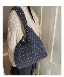 Detail of plush grey shoulder bag with white polka dots worn over a white knit sweater