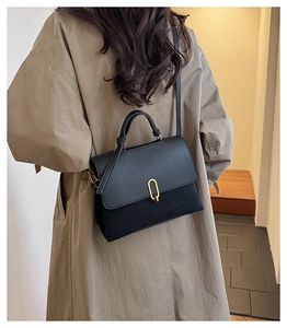 Detailed back view of a black patchwork handbag with gold U-shaped clasp worn as crossbody