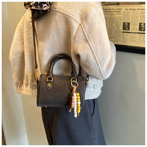 Detail der dunkelbraunen Boston-Tasche mit Perlenanhänger und Schultergurt