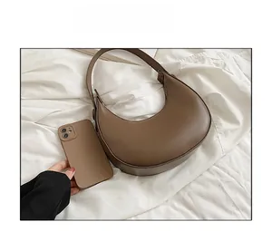 Brown leather crescent bag size comparison with smartphone on white fabric background