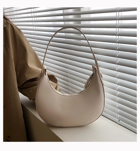 Detailed view of cream crescent bag with minimalist texture under window lighting