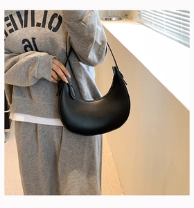 Detail view of a minimalist black crescent shoulder bag with smooth faux leather texture