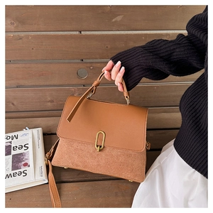 Brown leather handbag detail featuring textured panel stitching and a gold U-shaped buckle