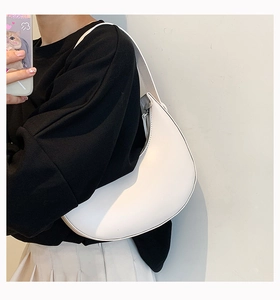 Minimalist white crescent shoulder bag in matte leather worn against a black outfit