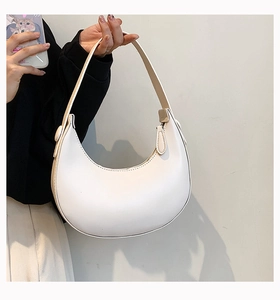 Detailed close-up of white leather crescent shoulder bag held by a model for size display