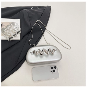 Silver metallic semi-oval evening bag with a wavy handle and chain strap on a desk