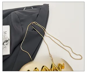 Close-up of golden acrylic clutch bag with metal wave decoration and snake chain strap