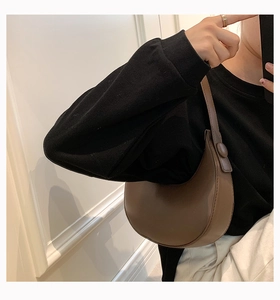 Close-up of brown crescent underarm bag in smooth leather worn by model on black hoodie