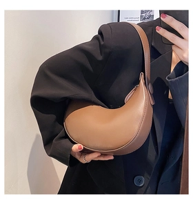 Detail of a brown crescent shoulder bag with decorative button on a model in a black suit