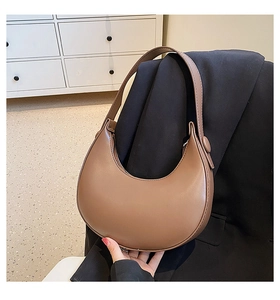 Brown leather crescent shoulder bag displayed against a minimalist office background