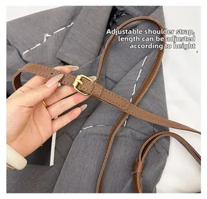 Detail of adjustable brown leather shoulder strap with gold buckle on a crossbody bag