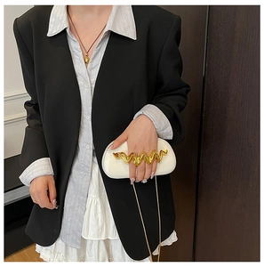 Detailed macro of white hardshell clutch bag with stylish wavy gold metal handle and chain
