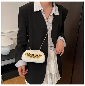 Detail of white semi-round crossbody bag with gold wave metal decor on a model