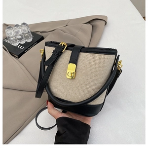 Chic beige woven bucket bag with black leather trim and a golden twist lock closure