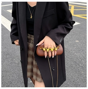 Detail of a brown leather clutch featuring a unique wavy gold metal handle and chain