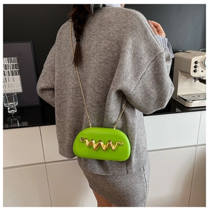 Detail of neon green crossbody bag with wavy gold buckle and metal chain strap