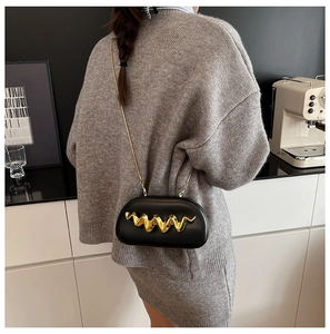 Detail of black capsule bag featuring bold gold wavy metal accent and fine chain strap