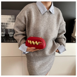 Chic red oval clutch bag featuring a gold wavy metal handle shown in a hand-held detail
