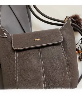 Close-up of litchi texture brown leather shoulder bag with white stitching and gold buckle