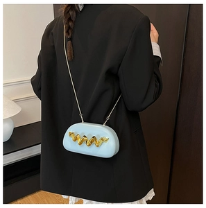 Detail of light blue oval handbag with wavy gold accent on a black blazer