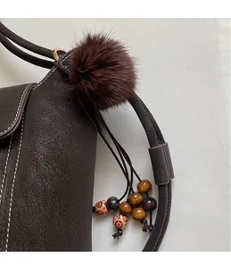 Detail of a brown plush ball charm with wooden beads on a stitched leather bag