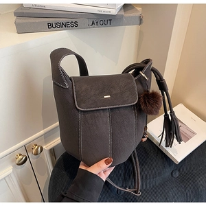 Detail of brown textured leather bucket bag with white stitching and tassel charm