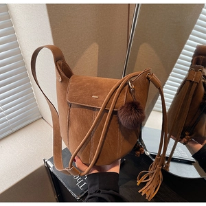 Detailed close-up of retro caramel brown matte leather bucket bag with fringe and pompom