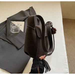 Detail of brown matte shoulder bag with white contrast stitching and a plush pompom charm