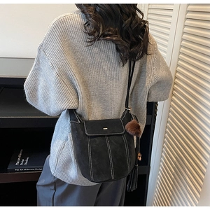 Detail of black crossbody bag with white stitching, plush ball and tassel accessories