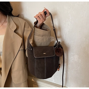 Detail of dark brown matte bucket bag with white contrast stitching and plush charm
