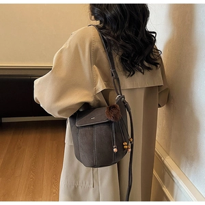 Detail of dark brown matte bucket bag with contrast stitching and plush ball charm