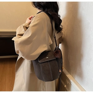 Detail of dark brown bucket bag with white stitching and plush charm on a khaki coat