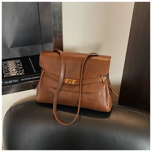 Detail of a brown leather tote bag showing a gold metal buckle and textured finish