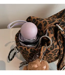 Detail view of large leopard print tote bag with folding umbrella and plush bear charm