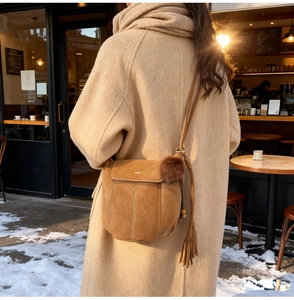 Detail of tan matte leather bucket bag featuring leather tassels and plush charm detail