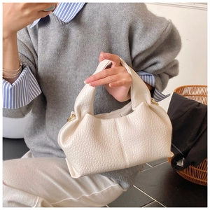 Detail of a creamy white textured leather dumpling bag with soft pleats and a wide handle