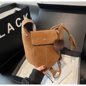 Close-up of brown frosted bucket bag with white decorative stitching and plush ball charm