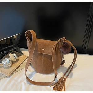 Detail of brown matte bucket bag featuring vintage tassels and a soft faux fur pompom charm