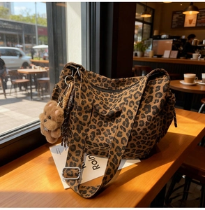 Detail of leopard print canvas bag with a cute plush bear charm on a wooden table