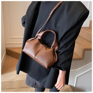 Deep brown cloud-shaped handbag with ostrich grain texture shown with black suit
