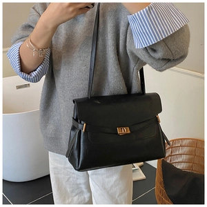 Close-up of a minimalist black tote bag with a golden rectangular metal buckle and flap