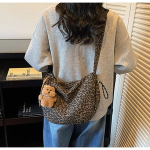 Detail of leopard print crossbody bag featuring a cute brown plush bear charm and wide strap