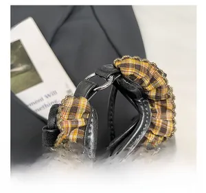 Close-up of the black leather handle with brown plaid ruffles and silver metal ring