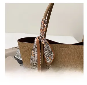 Detail of a geometric print silk scarf tied on a brown lychee leather tote bag handle