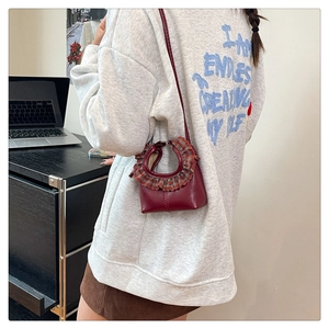 Close-up of burgundy mini crossbody bag with plaid ruffle trim worn by model in office