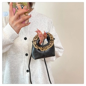 Detail view of mini black handbag featuring yellow plaid ruffle handle and shoulder strap
