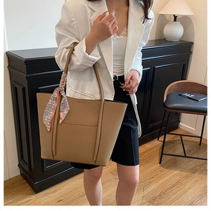 Detail of tan pebble leather tote bag with silk scarf handle on model in white blazer
