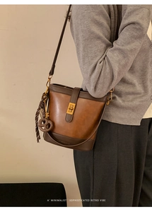 Détail du sac seau bicolore rétro avec boucle dorée et pendentif nœud porté par un mannequin